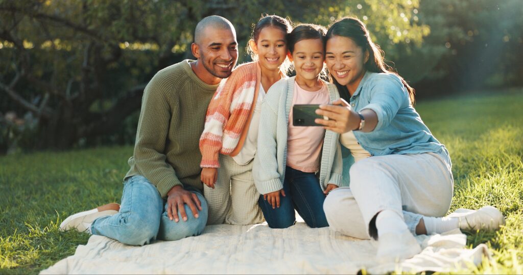 Selfie, mother and father with kids on picnic blanket for social media post, vacation and relax. Parents, children and family photo on grass for holiday, happy memory and profile picture at park